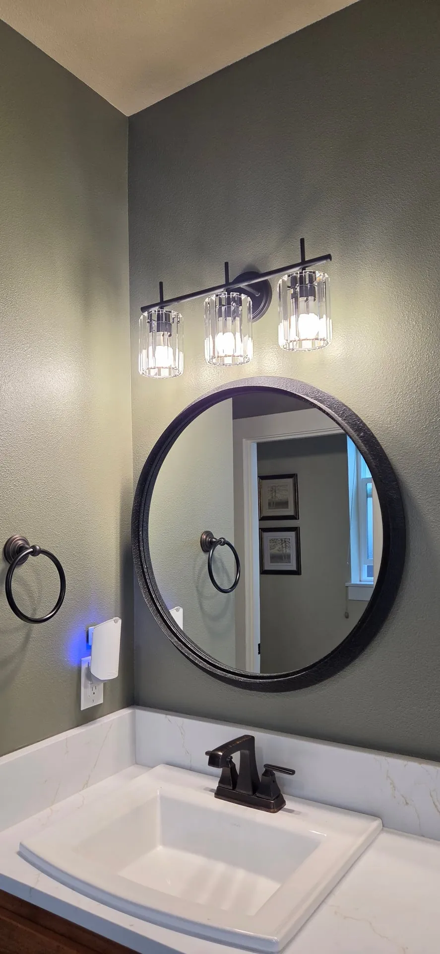New three-light crystal vanity fixture over a round black-framed mirror in a Vancouver WA bathroom after replacement