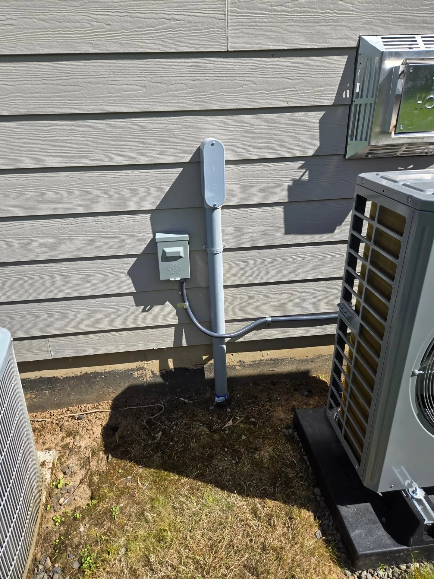 Ductless mini-split heat pump condenser mounted outside a Battle Ground WA home with a weatherproof electrical disconnect and conduit whip feeding the unit