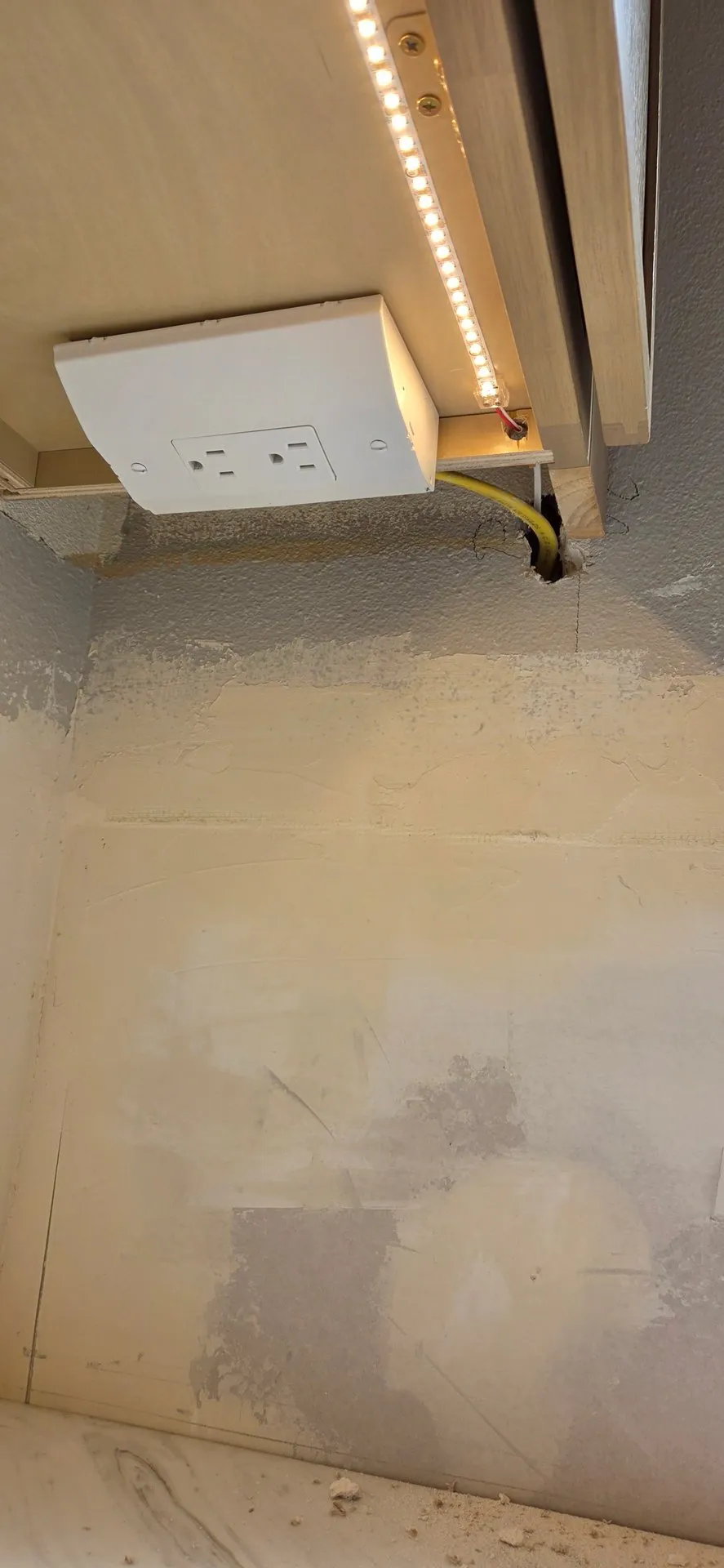 Yellow cable running out of a hole in the wall and into an under-cabinet outlet below an upper cabinet with an LED strip light in a Ridgefield WA kitchen