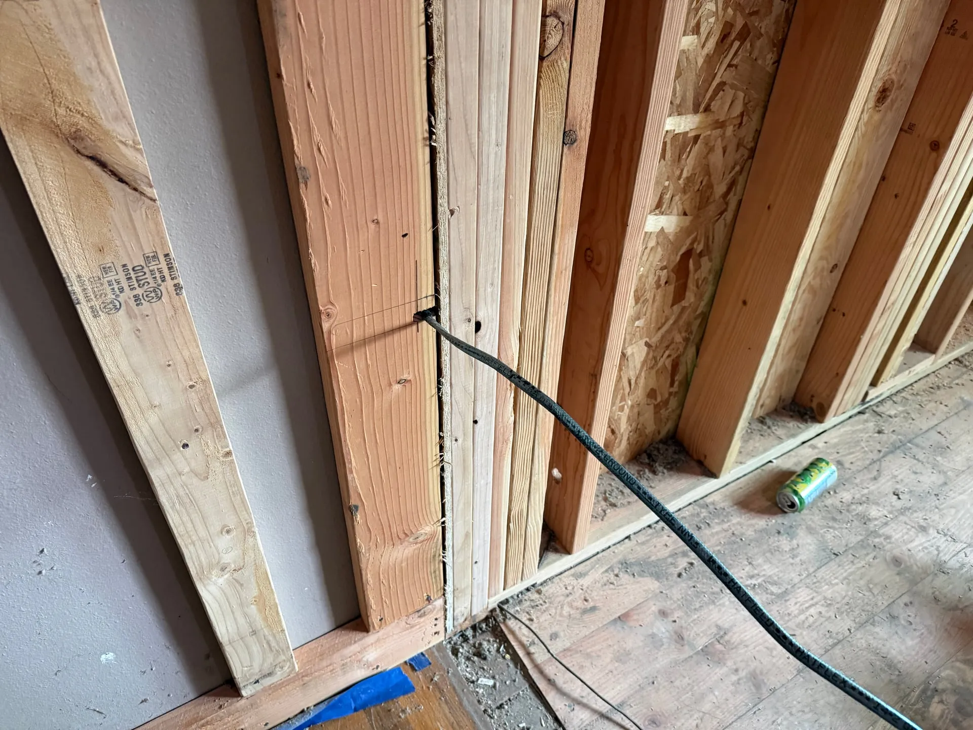 Black NM cable entering a drilled hole in new framing next to the existing drywall of an older Vancouver WA home during an addition rough-in