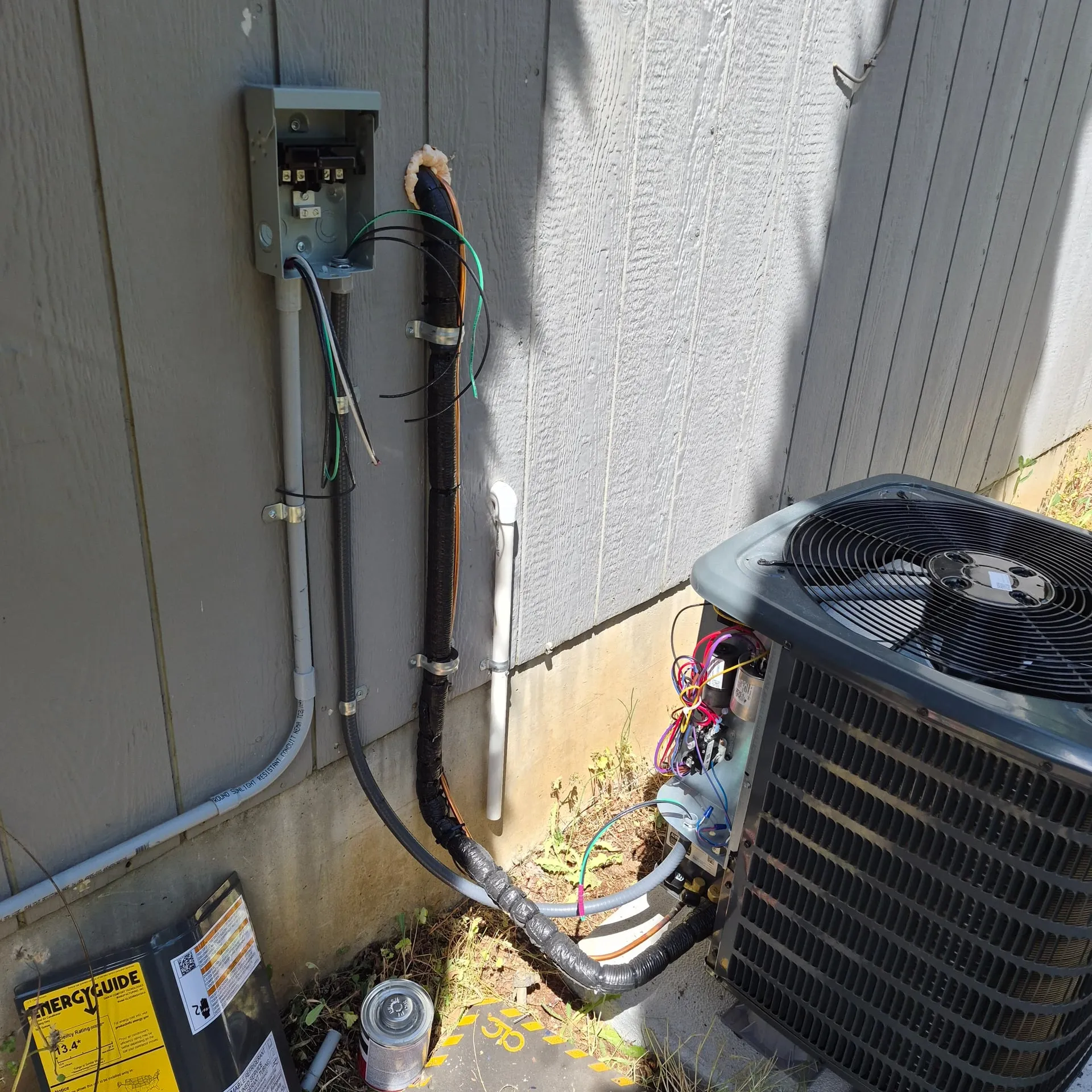 Open A/C disconnect being wired on the exterior wall of a Vancouver WA home, with line and load conductors, a green ground, and a taped sealtight whip routing down to the new condenser