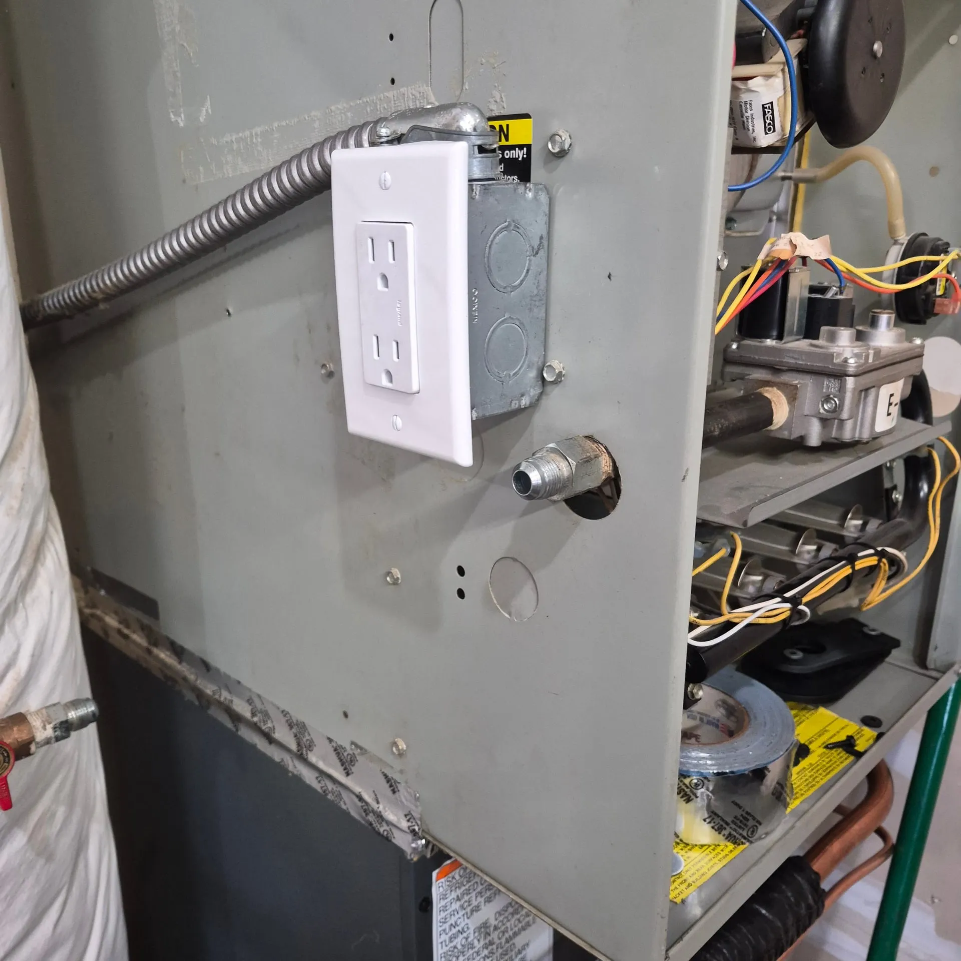 GFCI service receptacle mounted on a gas furnace cabinet in a Vancouver WA home with a flexible whip feed, the furnace burners and gas valve visible inside