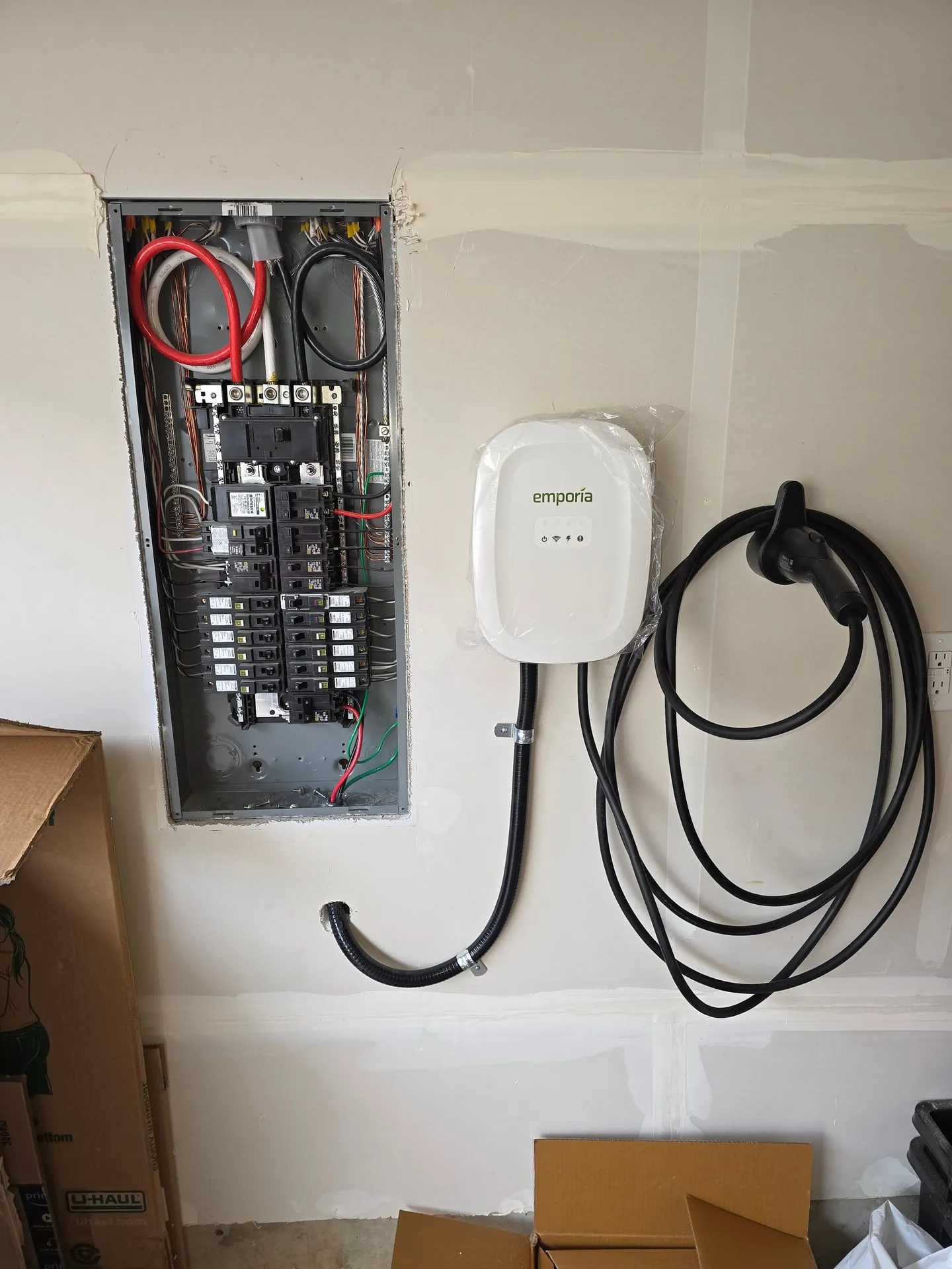 Main panel open with breakers exposed during the Emporia EV charger install in Hazel Dell, Vancouver WA, showing the short flexible metal conduit routed from the new 240V breaker to the charger base
