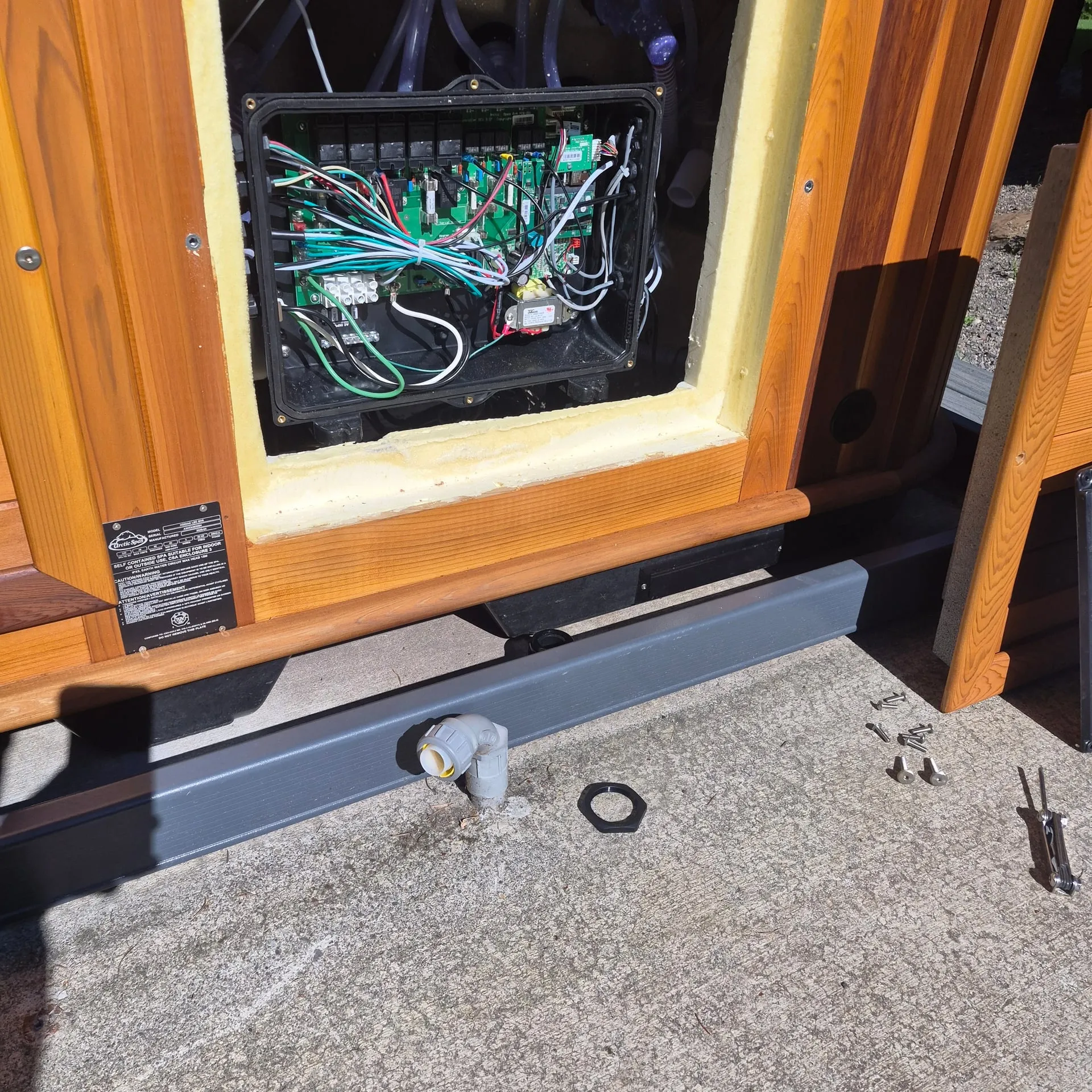 Liquidtight conduit whip and connector entering the spa pack of a cedar hot tub at a Brush Prairie WA home, the control board visible inside the open equipment bay