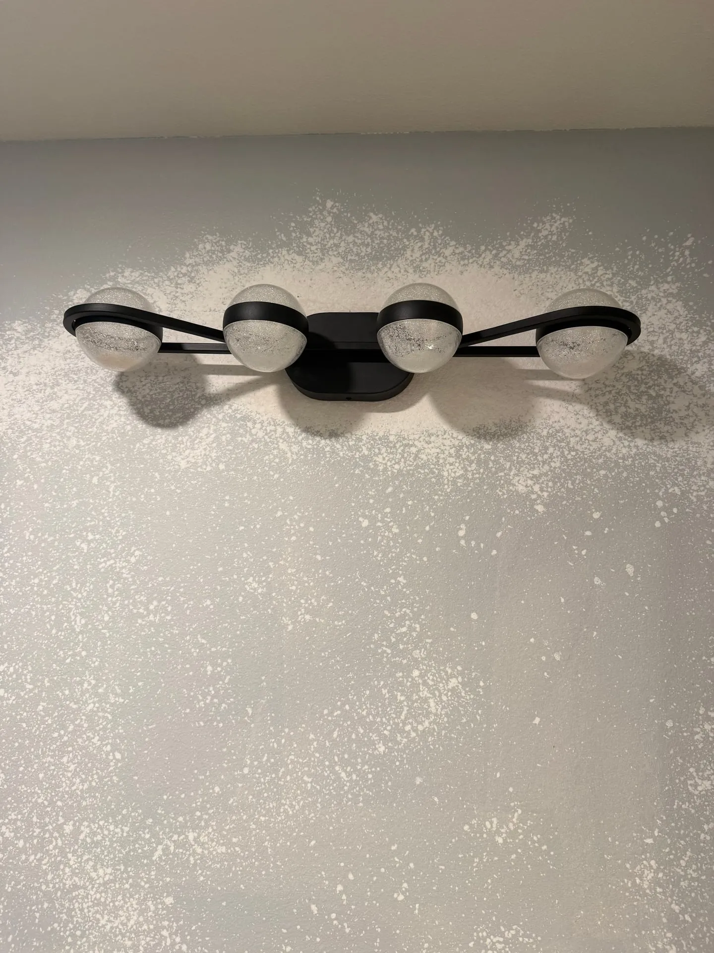 Modern 4-bulb black vanity light with globe shades installed on a textured gray wall in a remodeled bathroom in a Hazel Dell home