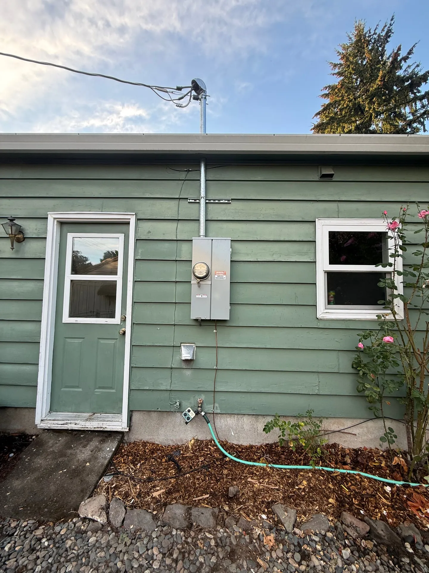 New 200-amp outdoor meter main combination panel on the green lap siding of a Vancouver WA home, with a new galvanized service mast and weatherhead above the roofline and the overhead service drop attached