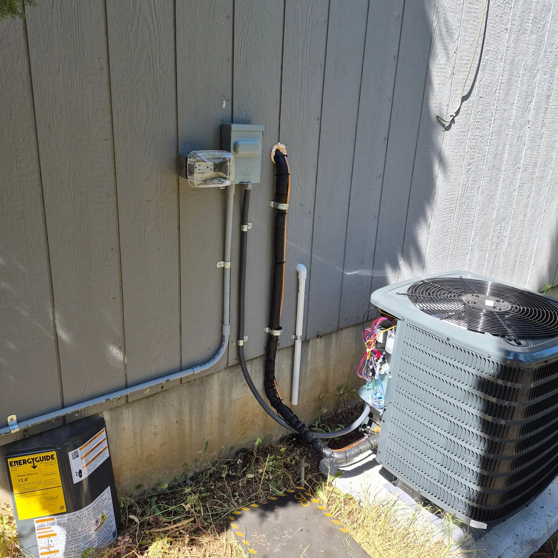 Finished outdoor A/C hookup at a Vancouver WA home with a new condenser, a wall-mounted weatherproof disconnect, a sealtight whip to the unit, and PVC conduit run neatly along the foundation