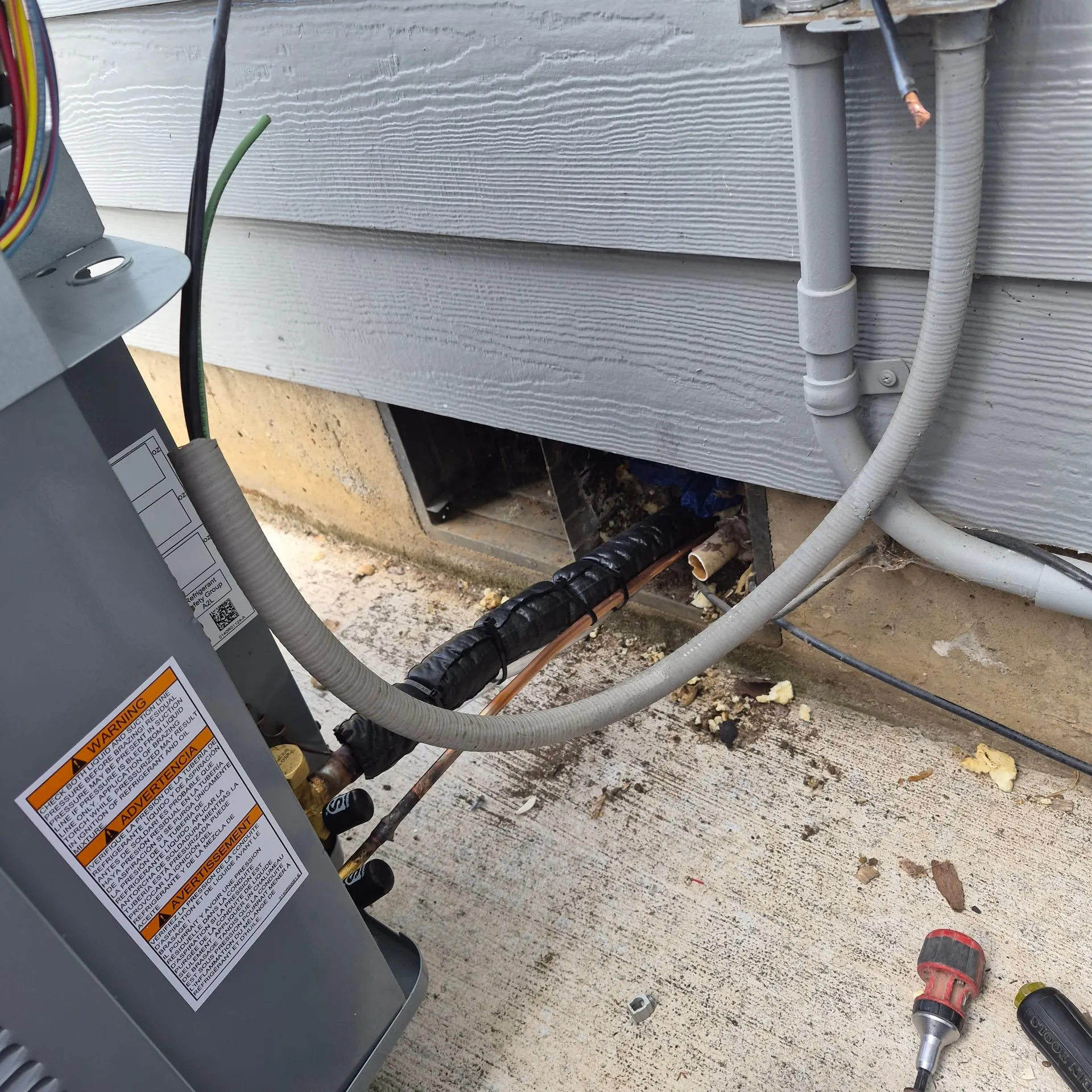 New outdoor A/C condenser hookup on the side of a Vancouver WA home in the Orchards area, with a gray weatherproof disconnect, a flexible sealtight whip feeding the unit, and the copper refrigerant lineset routed alongside
