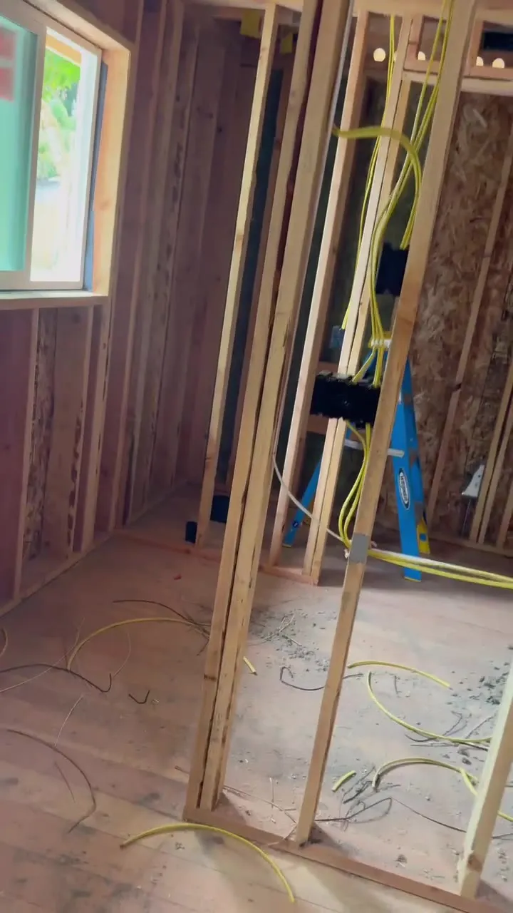 Open stud walls of a new bedroom addition in Vancouver WA during electrical rough-in, with bundles of yellow 12-gauge NM cable dropping to new device boxes and a window opening on the left