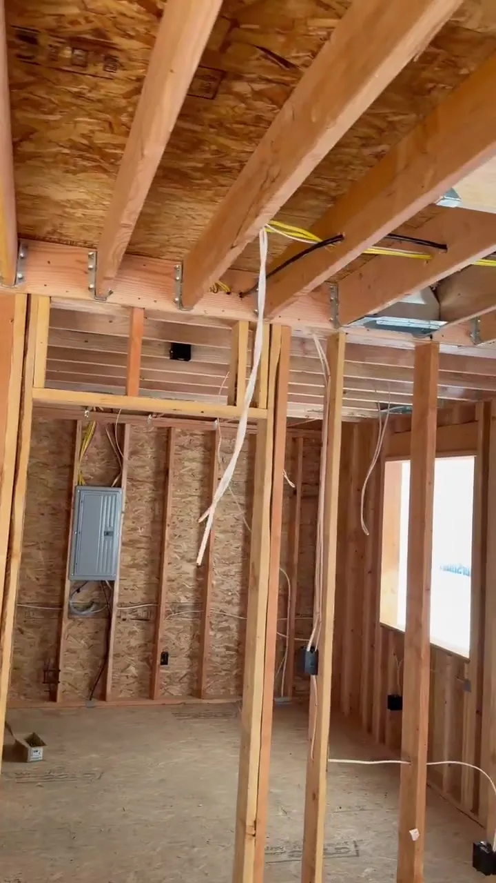 Open stud framing inside a new-construction ADU near Kalama WA during electrical rough-in, with the new electrical panel mounted on the far wall, NM cable home runs dropping from the ceiling joists and device boxes set on the studs