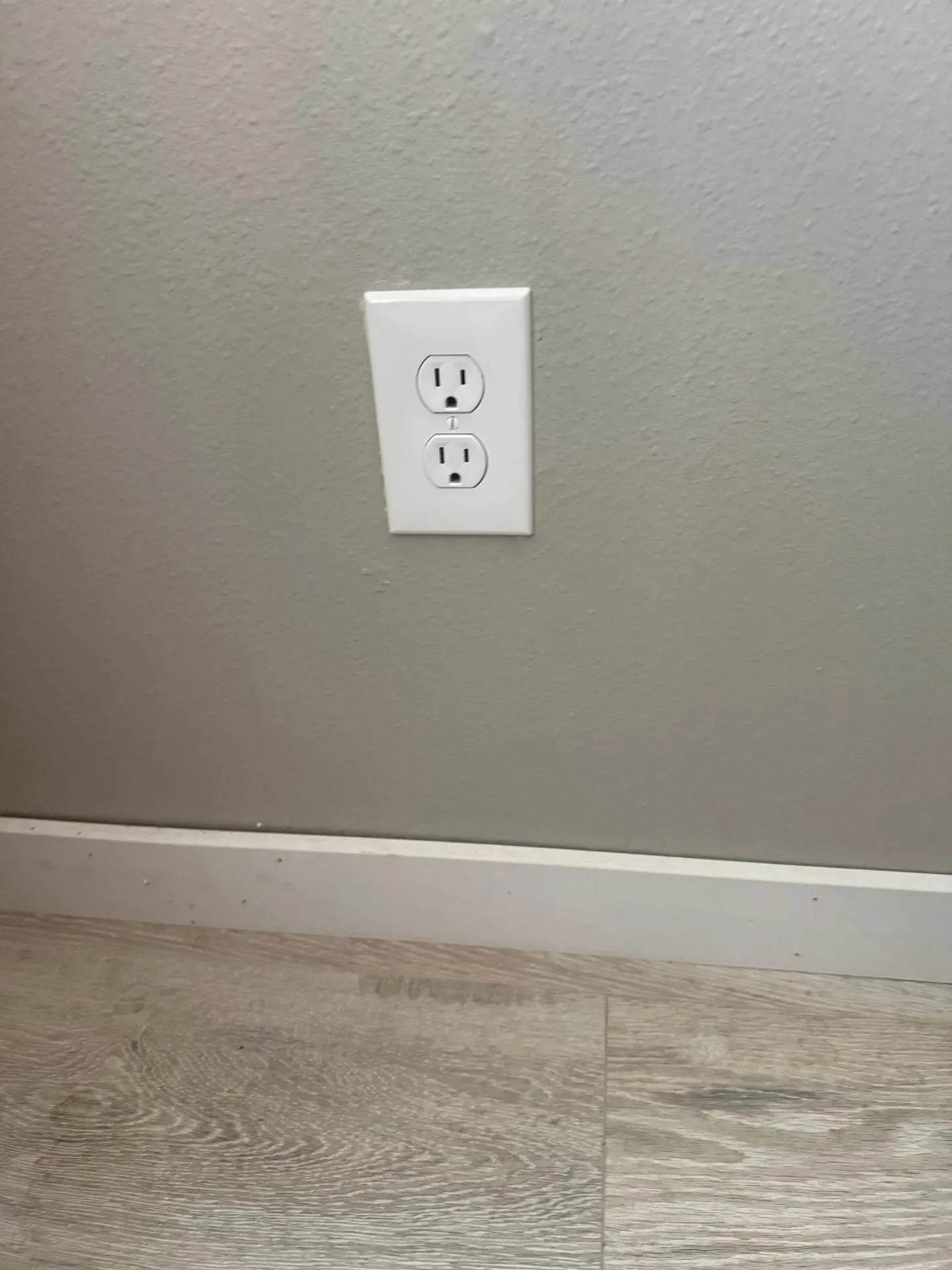 New white duplex receptacle and cover plate installed low on a gray wall above the baseboard in a Vancouver WA home