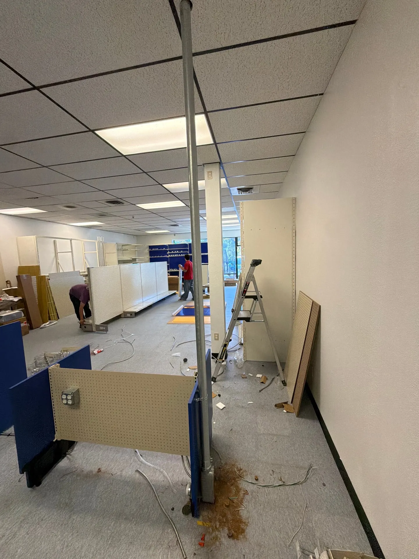 Wide view of a retail sales floor mid-buildout in Vancouver WA with an EMT power pole running from the ceiling to a gondola and fixture parts across the floor