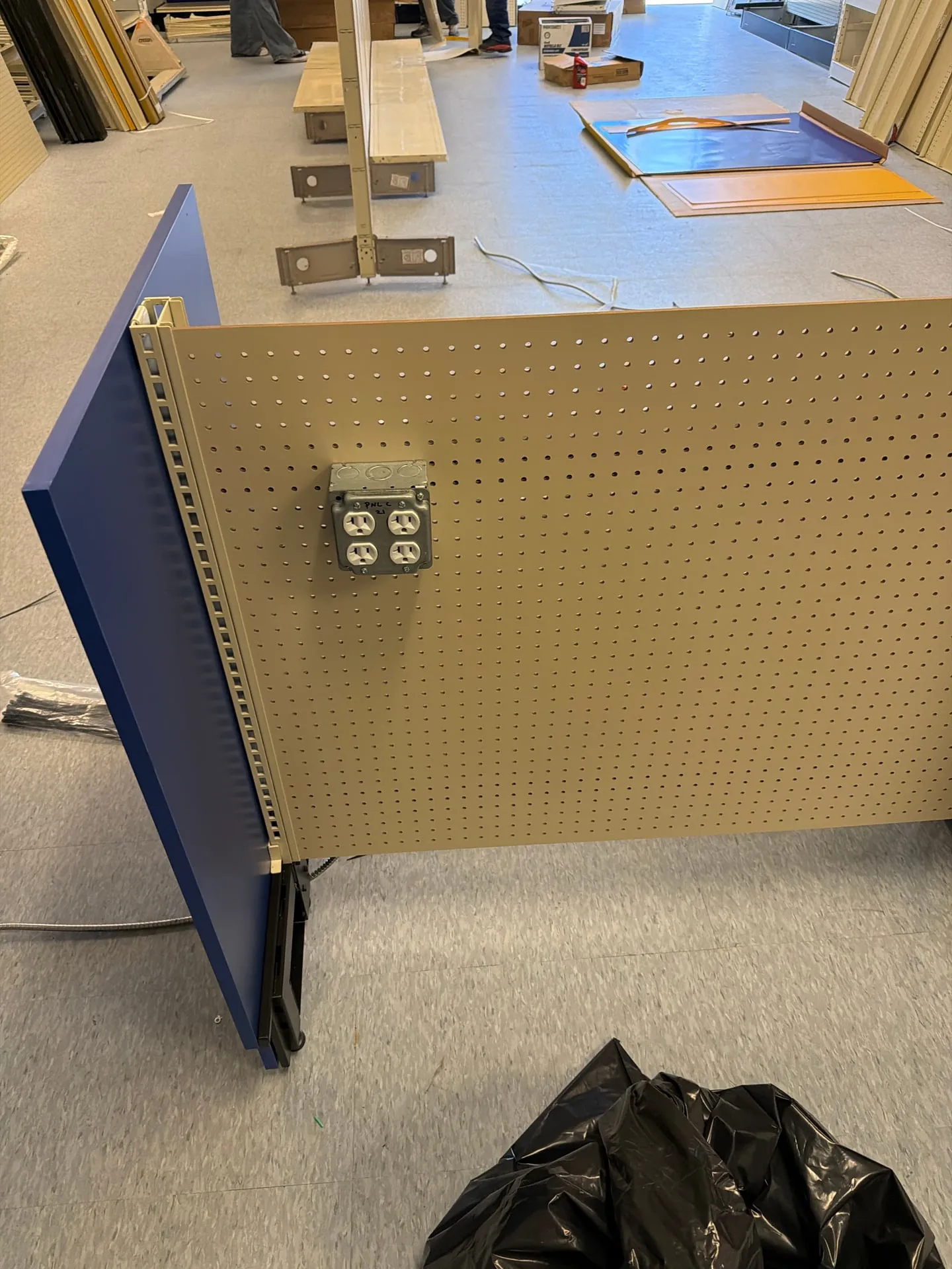 Quad receptacle in a metal box mounted on the tan pegboard back of a blue store gondola, with conduit fed in from the side