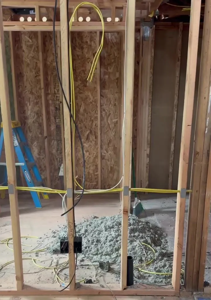 Studs of a new interior wall in a Vancouver WA addition with yellow NM cable run horizontally through drilled holes and steel nail plates on the stud faces, recessed light openings visible in the header above
